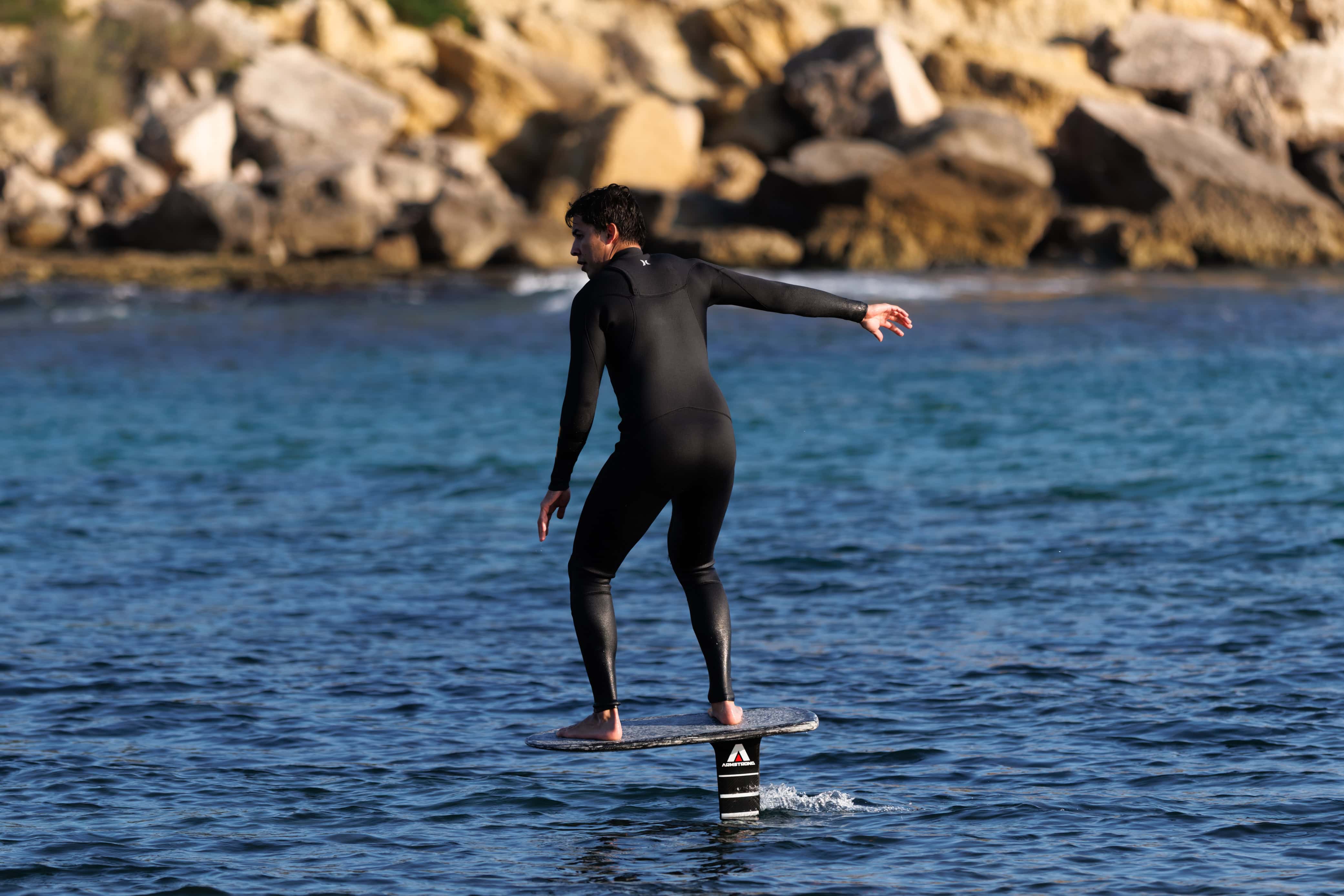 Surfeur en wetsuit sur une planche de foil en mer.