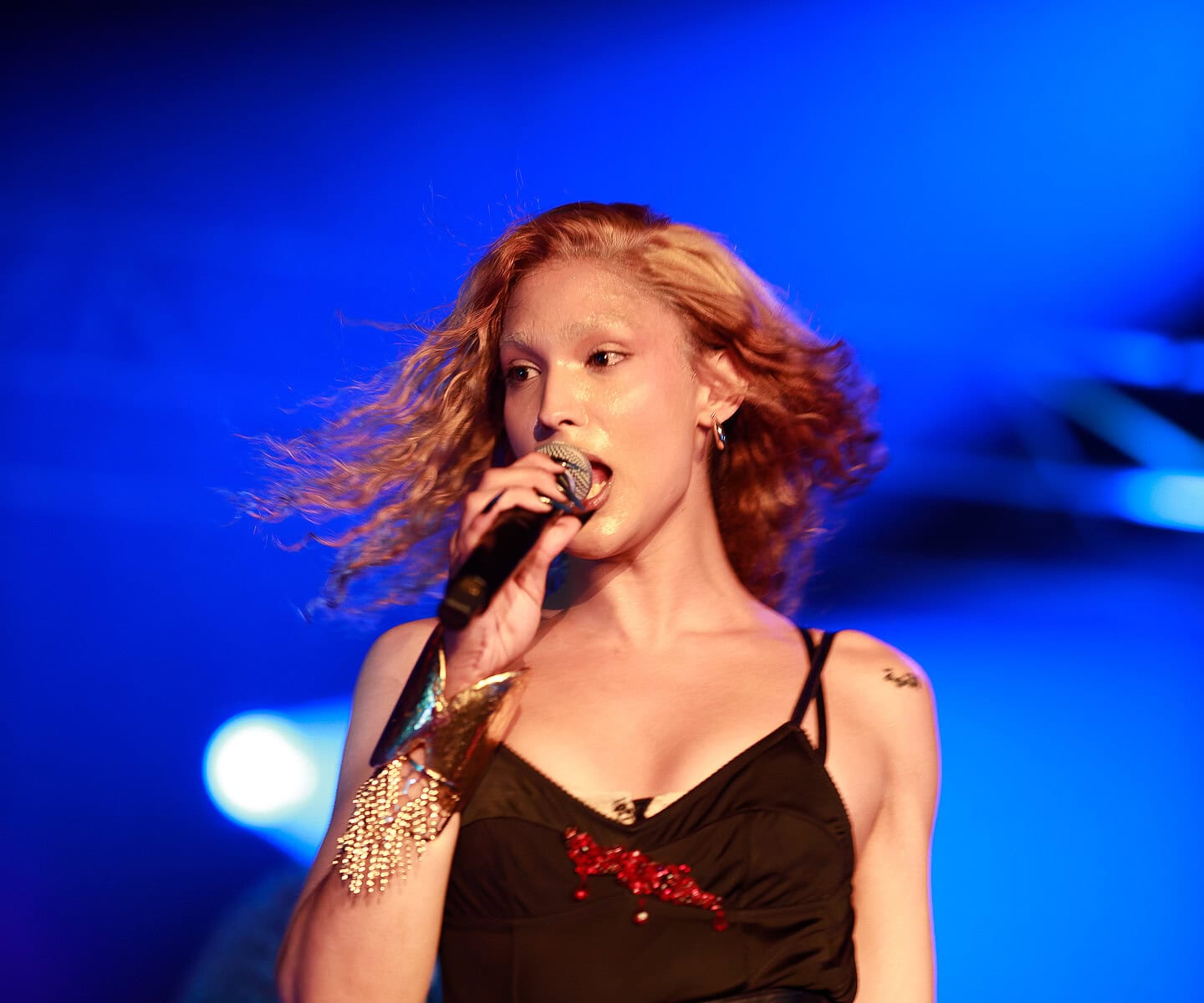 Jeune chanteuse sur scène lors d’un concert, portant une tenue noire élégante avec accessoires dorés.