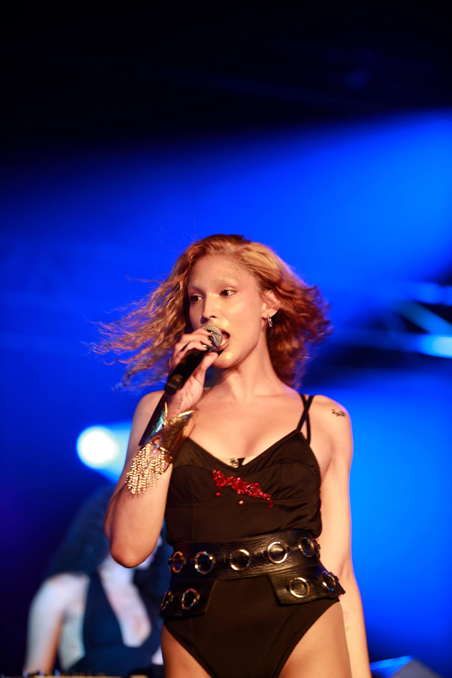Jeune chanteuse sur scène lors d’un concert, portant une tenue noire élégante avec accessoires dorés.