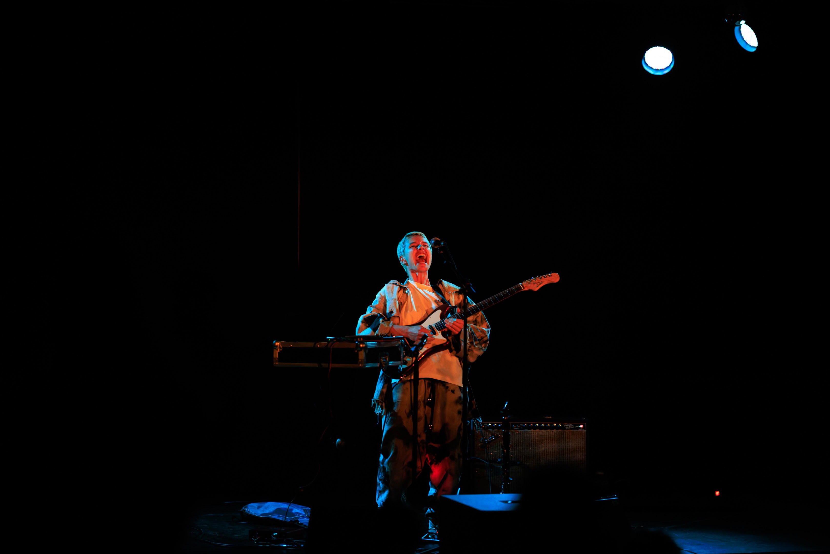 Musicien jouant de la guitare et du clavier lors d’un concert en scène sombre.